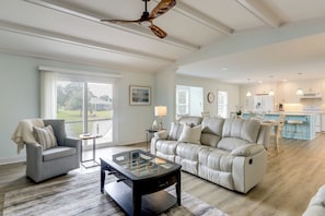 A spacious living room with a sofa, armchair, and coffee table. There is a kitchen area with a dining table and bar stools.