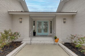 A building with a white brick facade, a blue door with glass panels, and a small porch with steps leading to the entrance. - White Heron Landing - Waterfront New Bern Home! (New Bern)