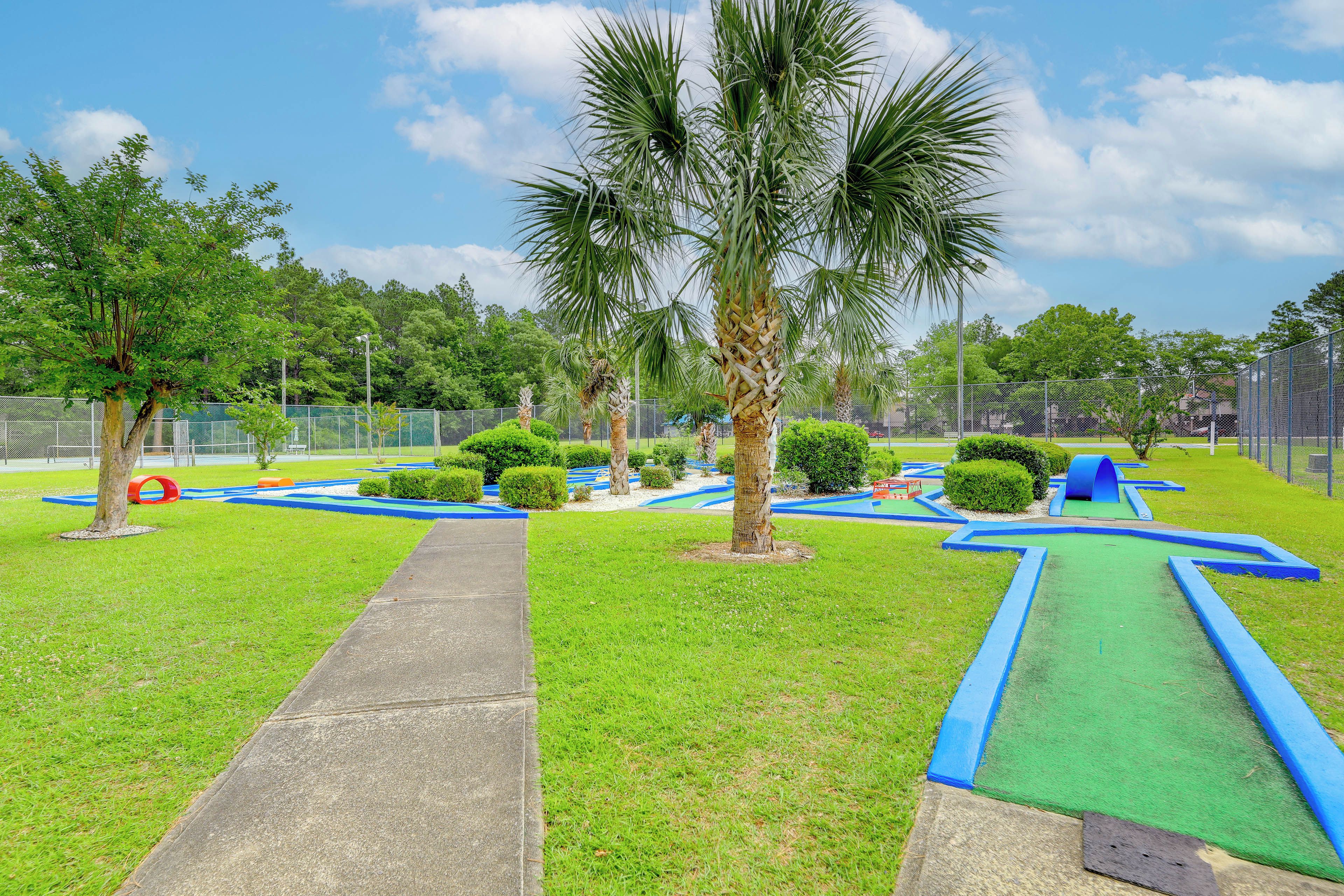 A well-maintained park with a clear pathway, palm trees, and a blue play area.