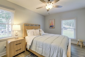A bedroom with a bed, nightstand, lamp, ceiling fan, and two windows.