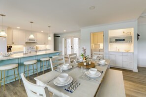 A modern kitchen with white cabinets, a central island with stools, and a dining area set for six with white tableware.
