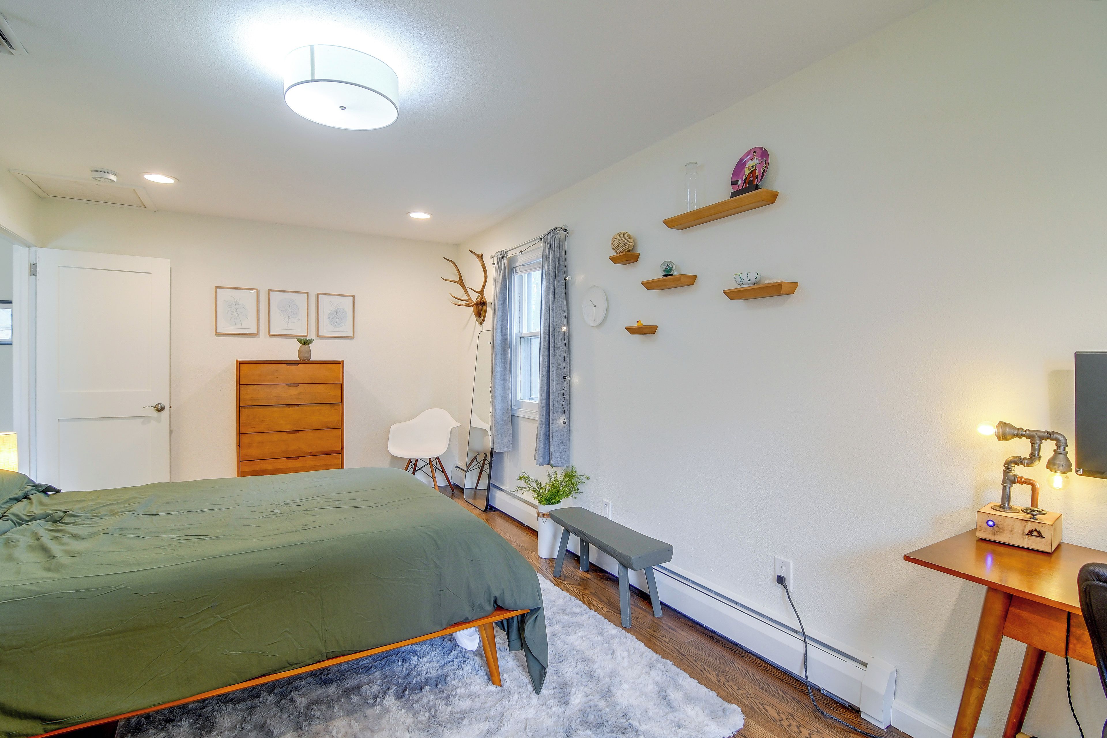 Un dormitorio con cama, escritorio, silla, espejo y ventana con cortinas.