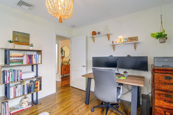 A home office with a desk, two monitors, a bookshelf, and a hanging plant.