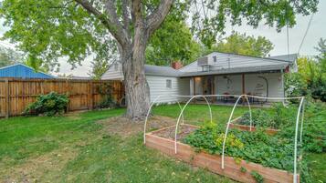 A residential backyard with a wooden deck, a large tree, and a raised garden bed.
