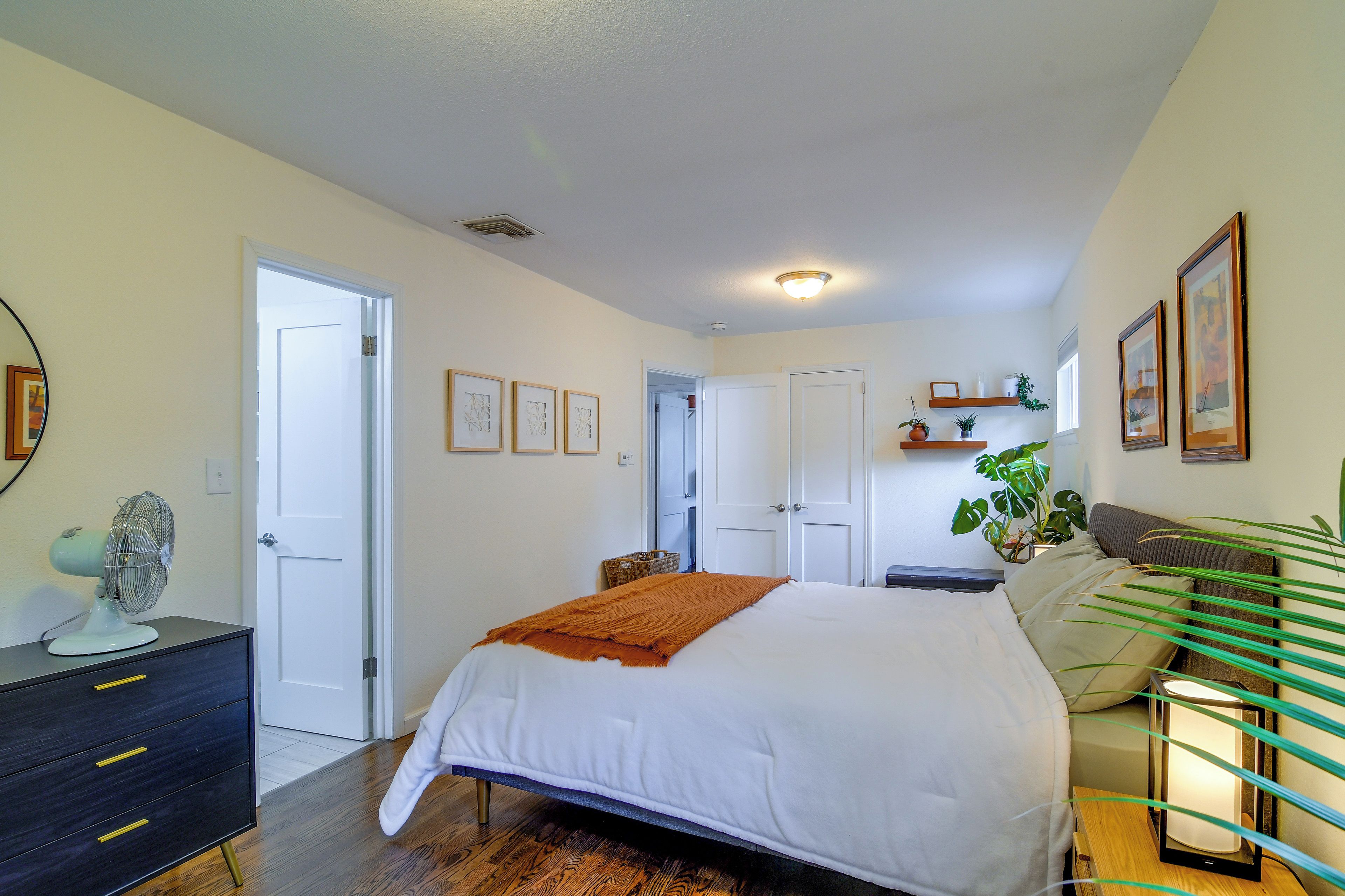 A bedroom with a bed, bedside tables, a dresser, a mirror, and a ceiling fan.