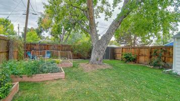 A backyard with a large tree, raised garden beds, and a wooden fence.