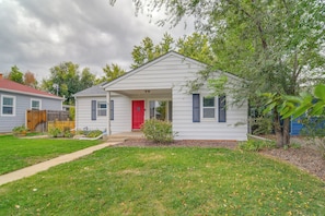 A single-story house with a red front door, a small porch, and a yard with grass and trees.