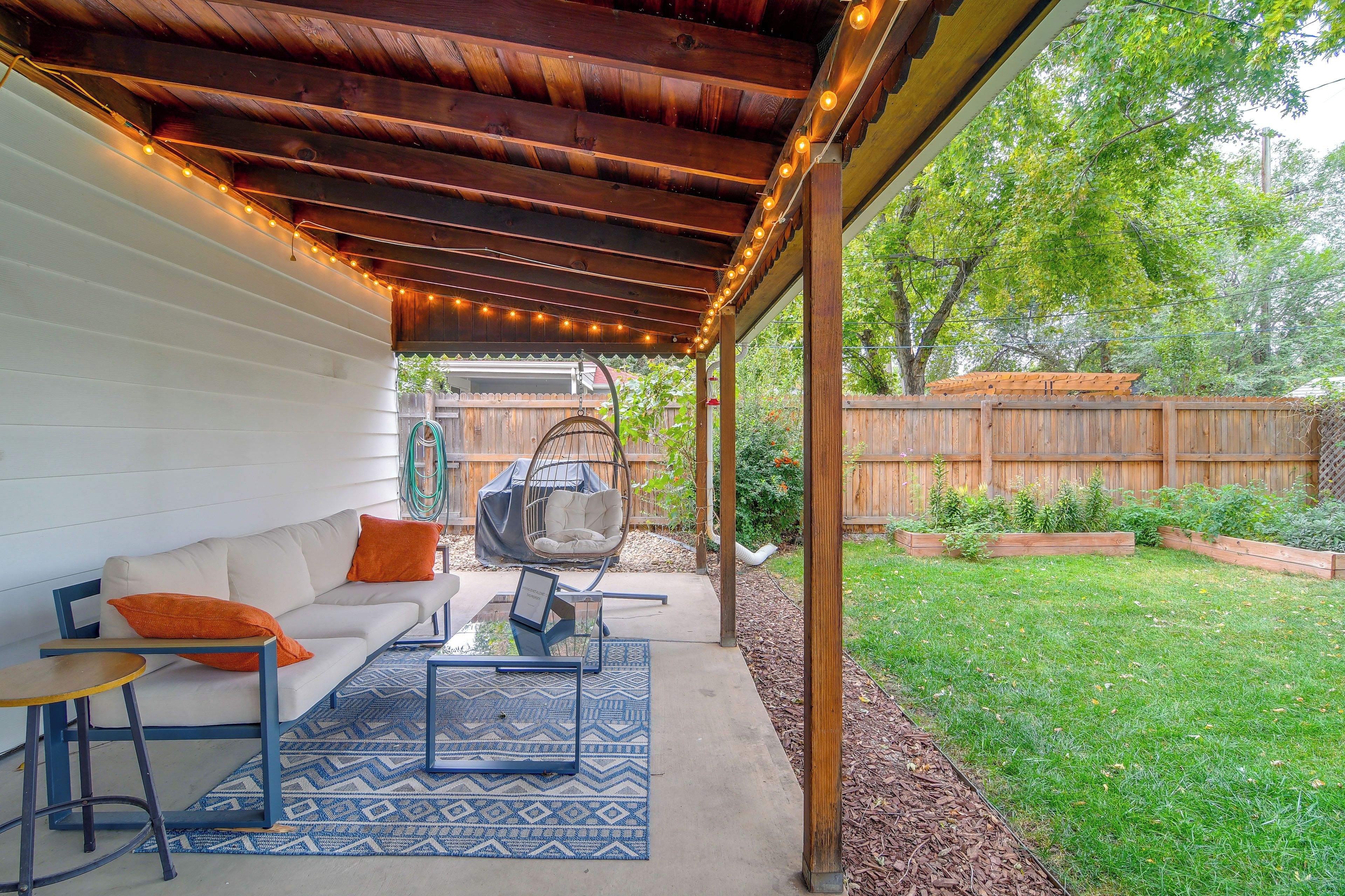 A covered patio area with a sofa, a hanging chair, and a table with a rug.