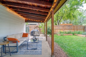 A covered patio area with a sofa, a hanging chair, and a table with a rug.