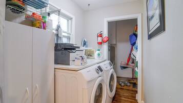 A laundry room with a washing machine, dryer, ironing board, and various cleaning supplies.