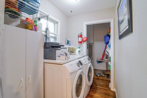 A laundry room with a washing machine, dryer, ironing board, and various cleaning supplies.
