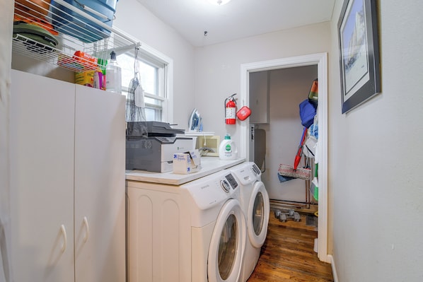 A laundry room with a washing machine, dryer, ironing board, and various cleaning supplies.