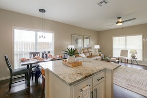 A modern kitchen with a central island, dining area with chairs, and a living room with a sofa. - Walk to Texas A&m! Quiet Home w/ Fenced Yard (College Station)