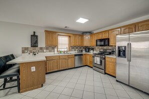 A modern kitchen with wooden cabinets, stainless steel appliances, and a tiled floor.