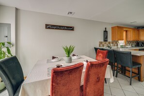 A dining area with a table set for four, surrounded by chairs, a potted plant, and a wall-mounted sign.