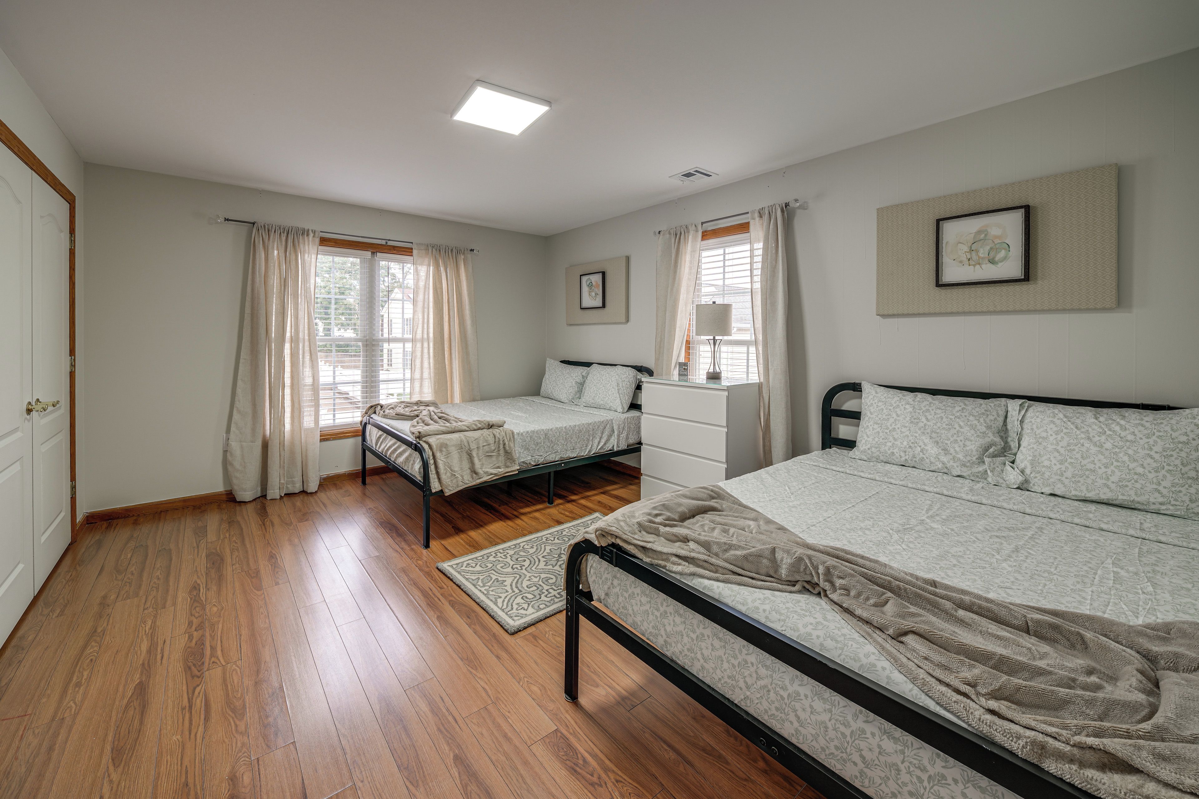 A bedroom with two beds, a window with curtains, a radiator, and a framed picture on the wall.