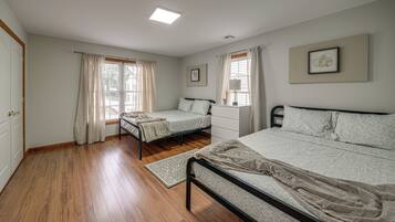 A bedroom with two beds, a window with curtains, a radiator, and a framed picture on the wall.