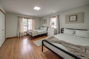 A bedroom with two beds, a window with curtains, a radiator, and a framed picture on the wall.