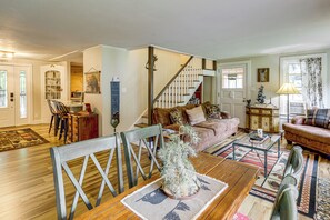 A cozy living room with a wooden dining table, a sofa, and a staircase leading to another level. - 1/2 Mi to Marina! Lake George Group Getaway (Diamond Point)