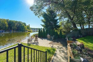 Un patio junto al río con mobiliario exterior, una valla de madera y una zona ajardinada.