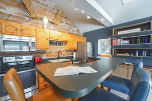 A kitchen with wooden cabinets, stainless steel appliances, and a central island with a book on it. - Dock + Year-round Fishing! Lakefront Michigan Home (Newaygo)