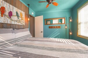 Un dormitorio con cama, ventilador de techo, espejo en la pared y ventana con persianas.