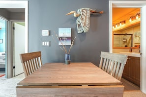 Een eethoek met een houten tafel, stoelen, een vaas met takken en een kunstwerk aan de muur.