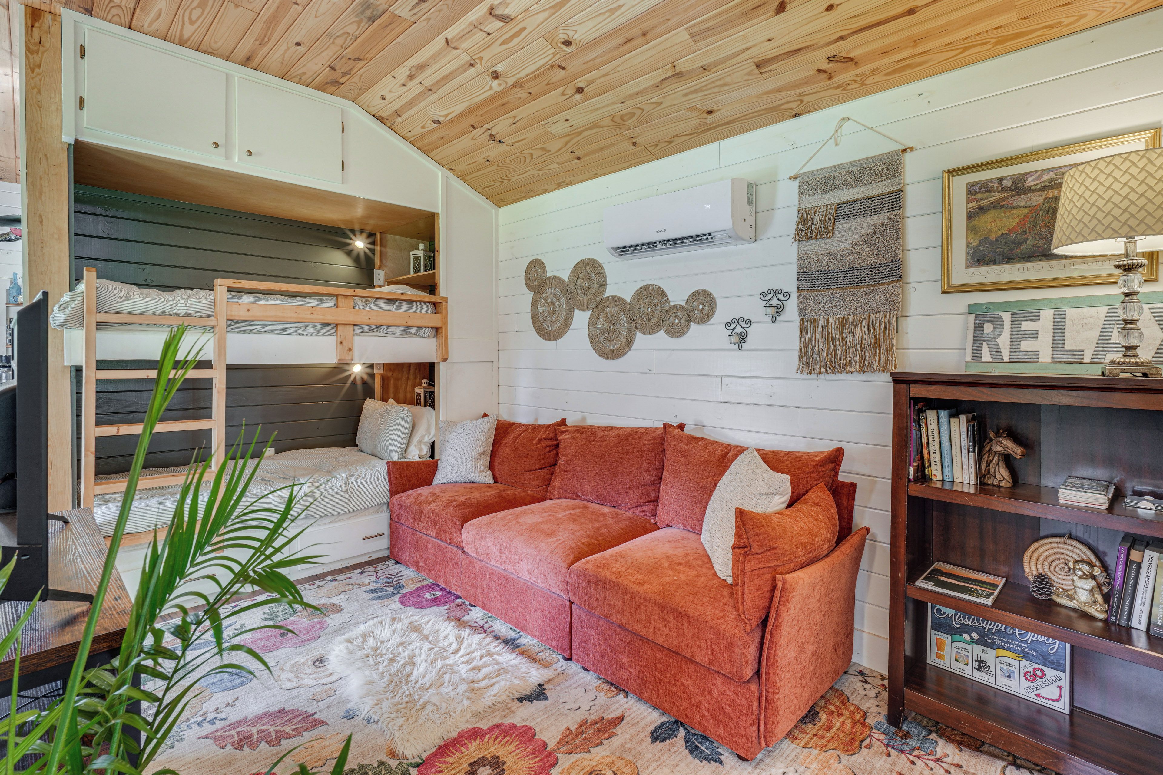A cozy room with a bunk bed, a red sofa, a bookshelf, and a decorative wall.