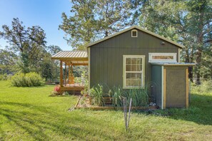 A small wooden shed with a window, surrounded by a grassy area with plants and trees.