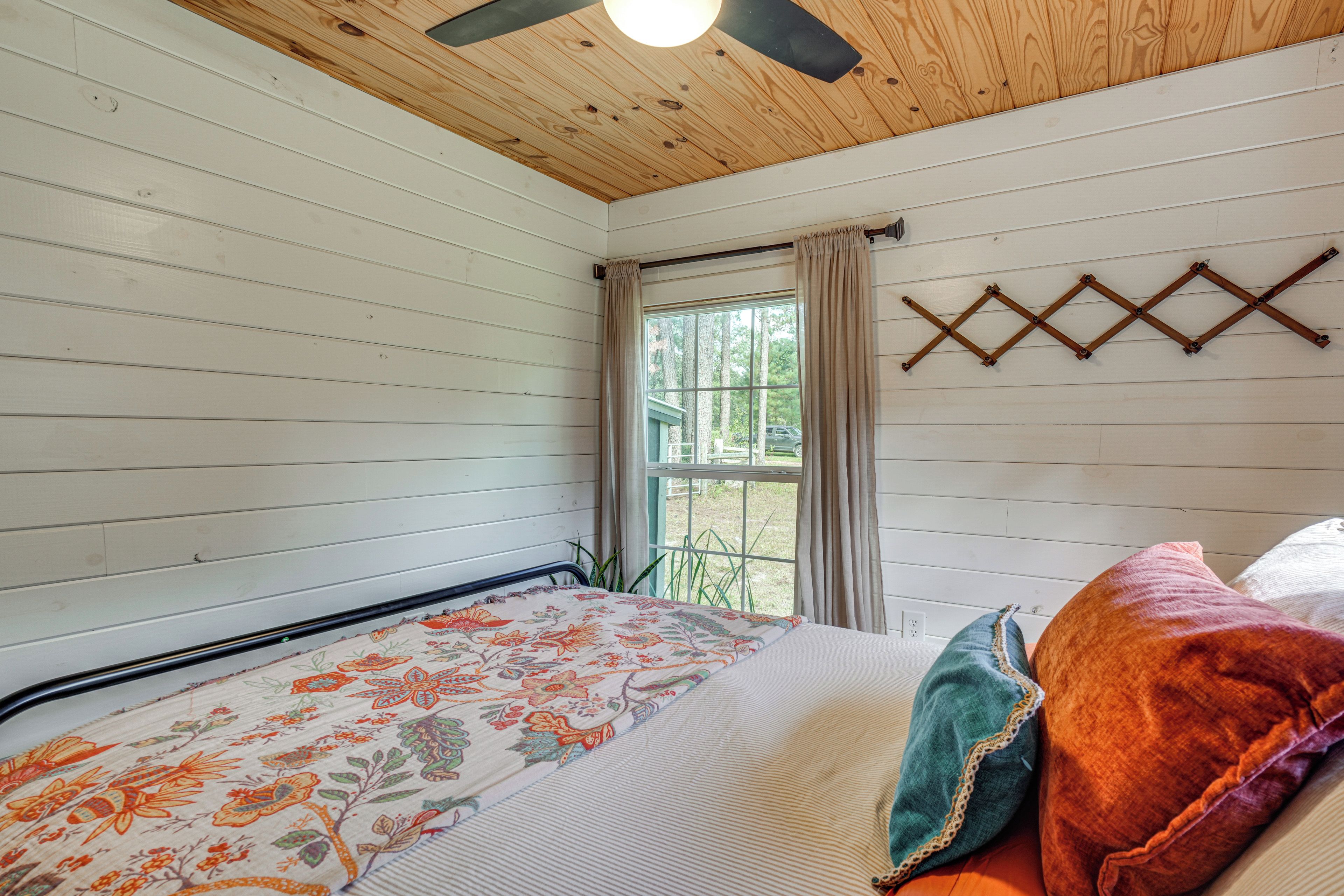 A room with a bed, a window with curtains, a ceiling fan, and a wall-mounted light fixture.