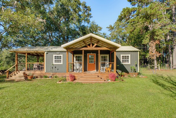 A two-story cabin with a front porch, wooden stairs, and a fenced yard.