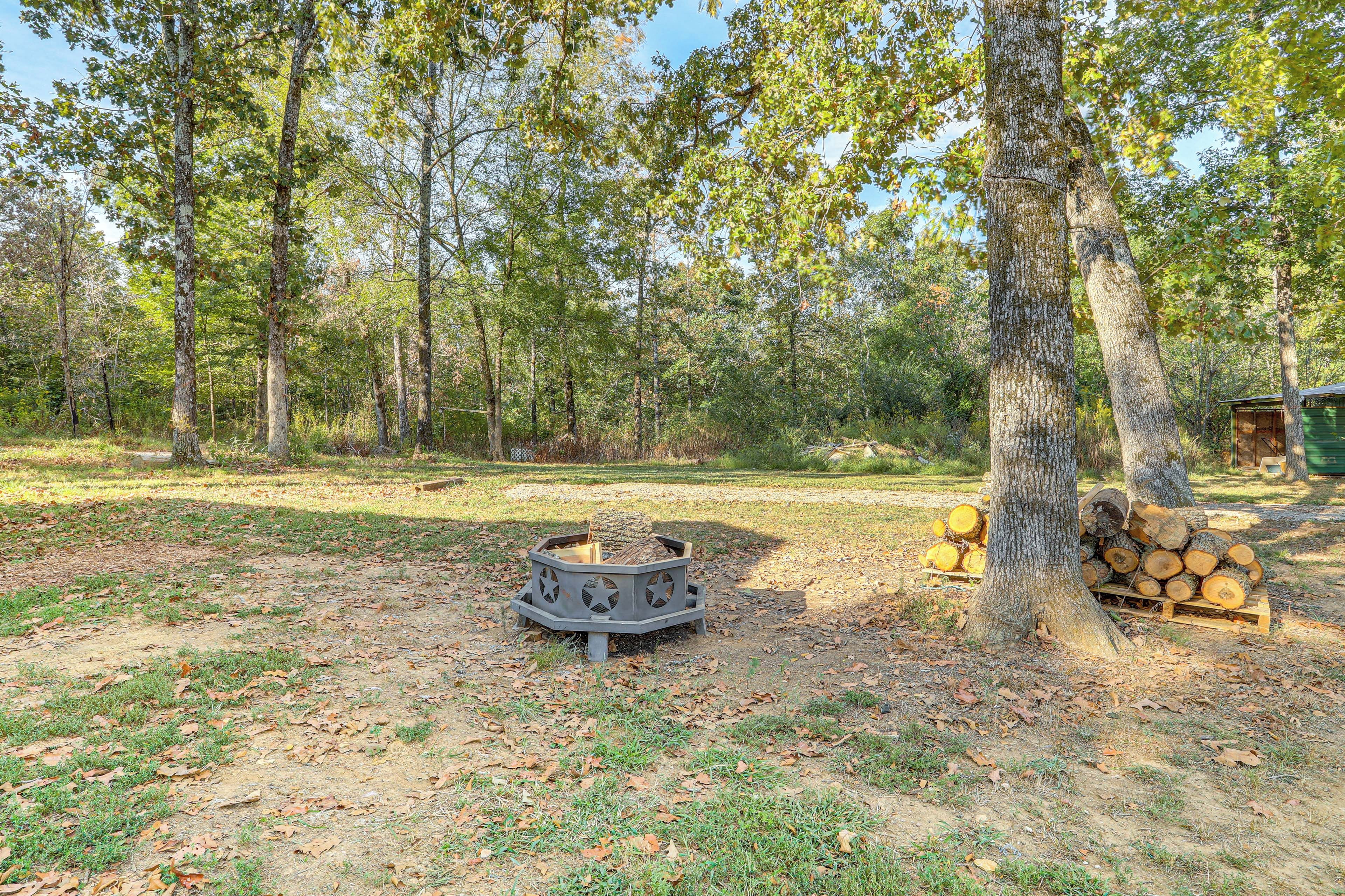 A forested area with a fire pit and a stack of firewood.