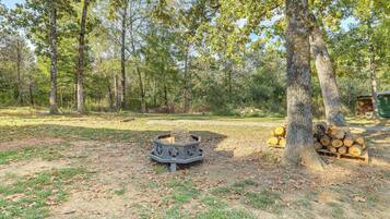 A forested area with a fire pit and a stack of firewood.