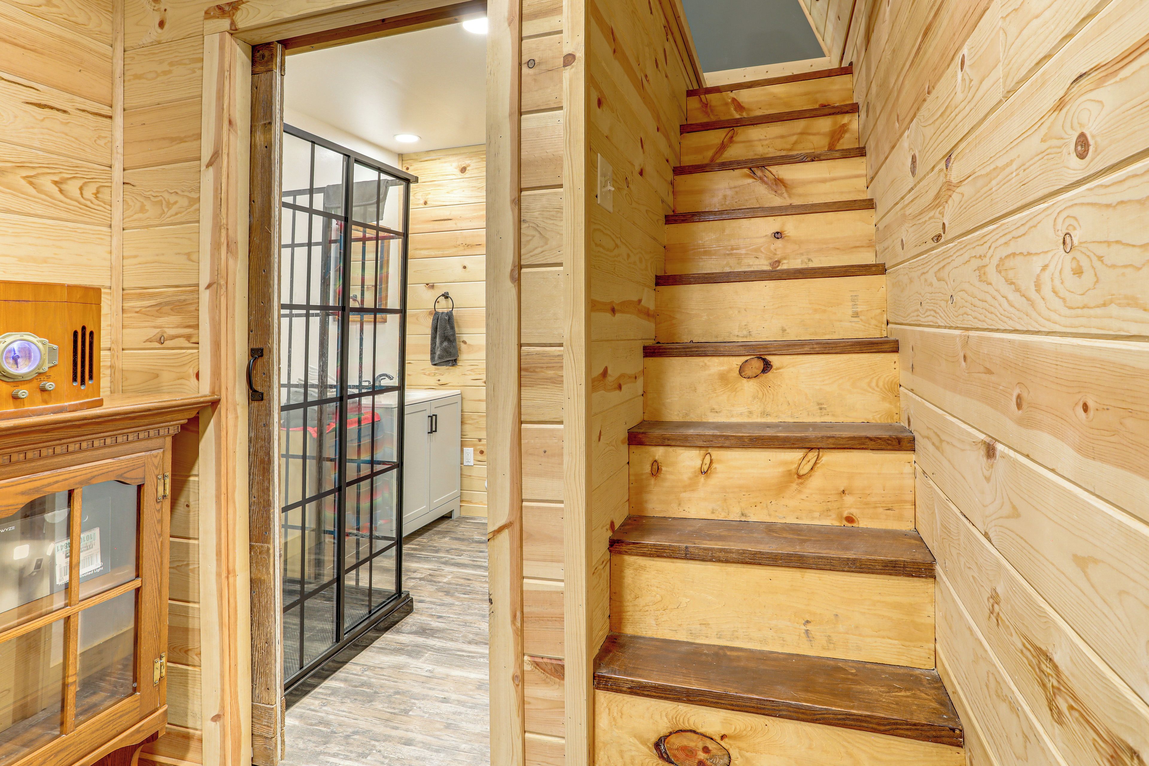 A wooden interior with a staircase, a glass door leading to a room, and a wooden cabinet with a light fixture.