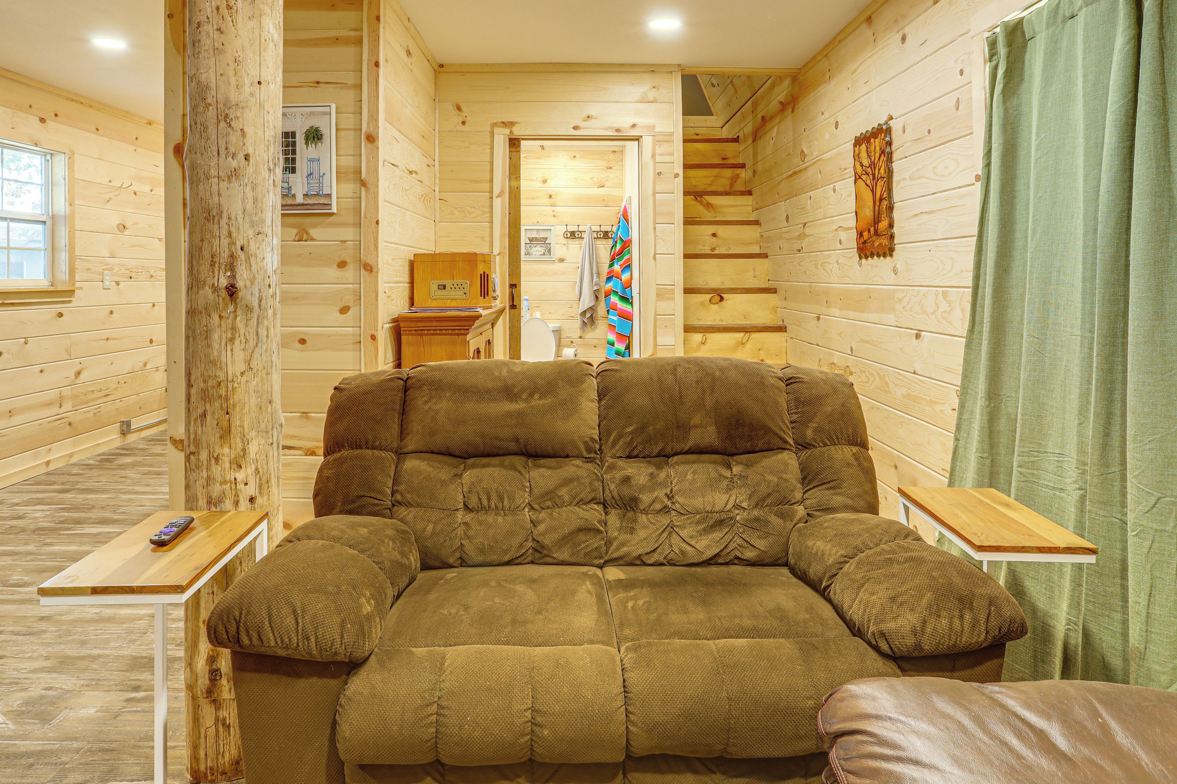 A cozy log cabin interior with a large cushioned sofa, wooden walls, a small table, and a green curtain.