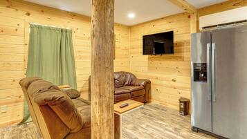 A cozy room with a brown leather sofa, a small wooden table, a television mounted on the wall, and a stainless steel refrigerator.