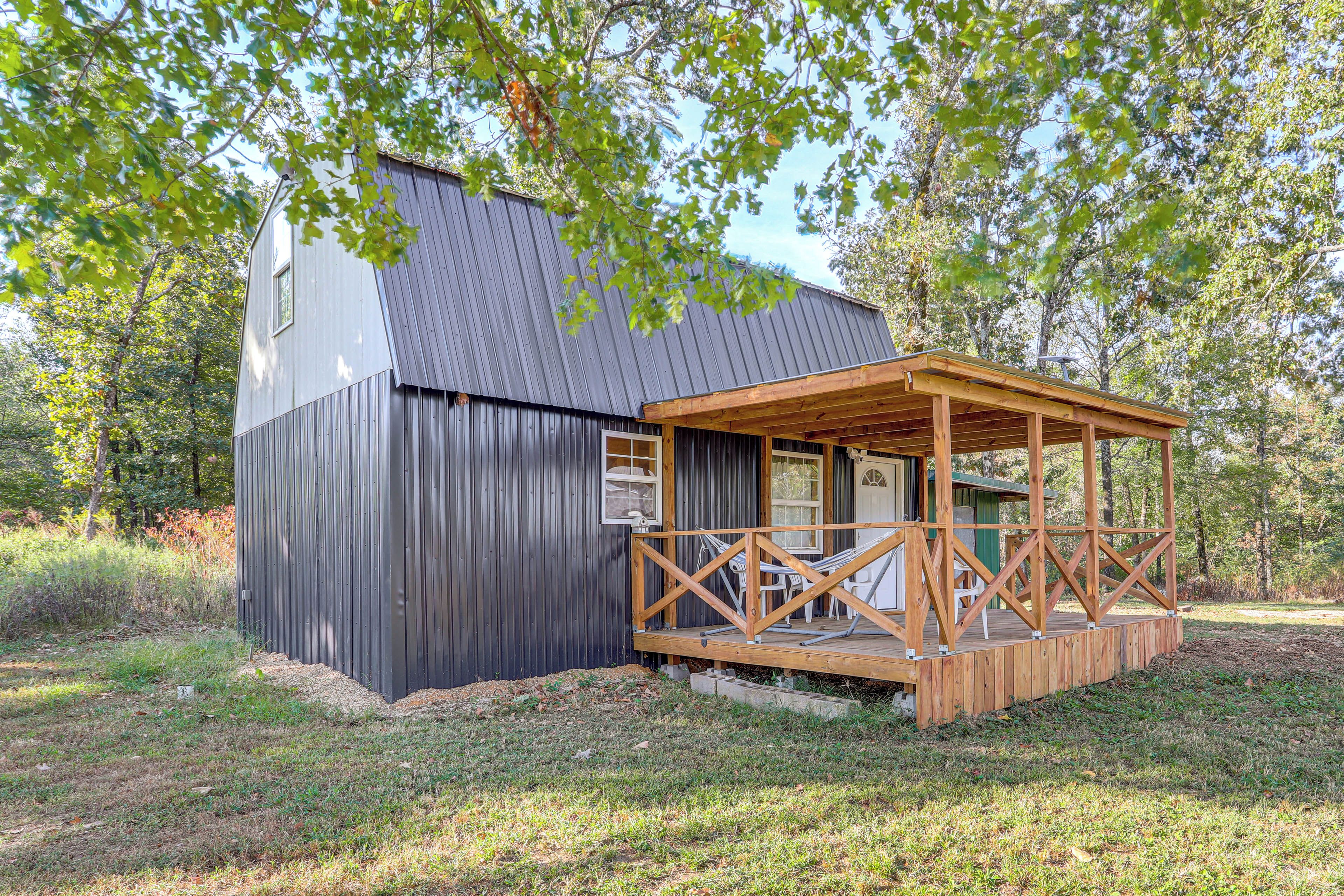 A small wooden cabin with a metal roof, a porch with a railing, and a door leading to the interior.