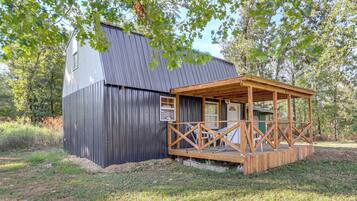 A small wooden cabin with a metal roof, a porch with a railing, and a door leading to the interior.