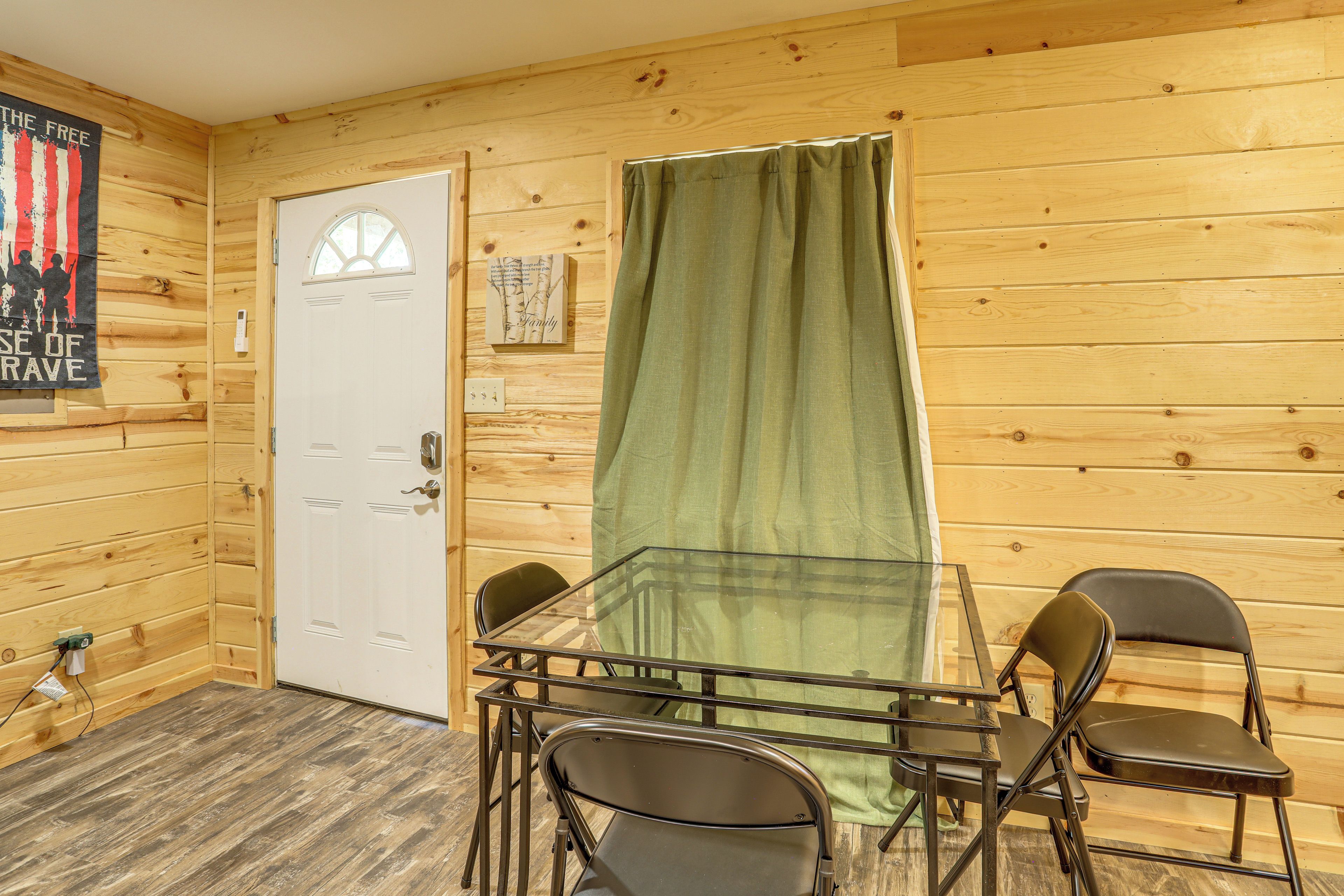 A room with a wooden interior, a white door, a glass table with chairs, and a green curtain.