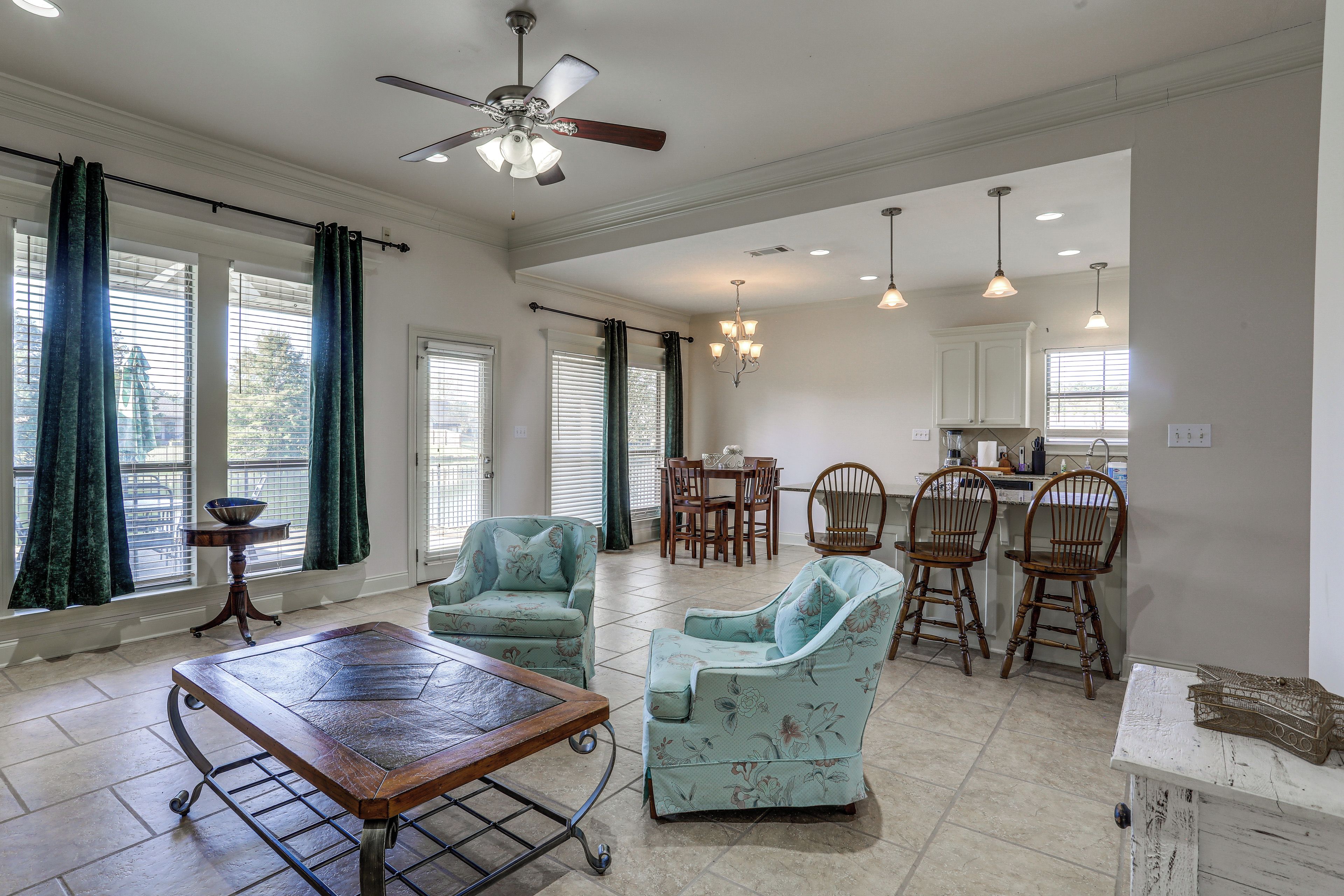 A spacious living area with a dining set, a ceiling fan, and a kitchen area with pendant lights.