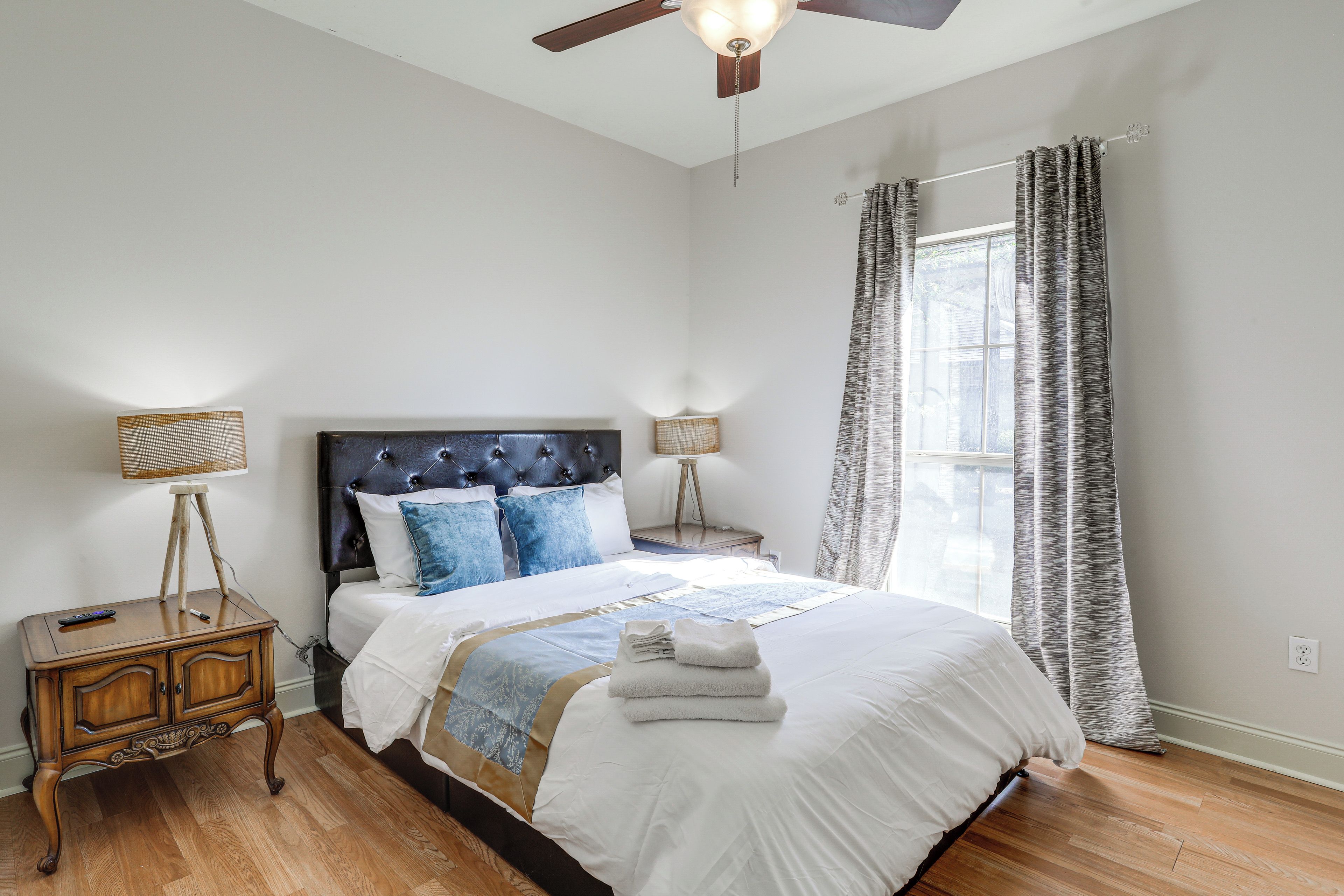A bedroom with a large bed, a nightstand, a lamp, and a ceiling fan.