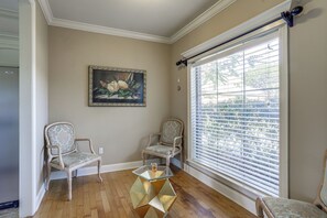 A room with two upholstered chairs, a glass coffee table, a painting on the wall, and a window with blinds.