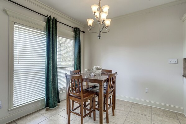 A dining area with a table, chairs, a chandelier, and a window with blinds and curtains.