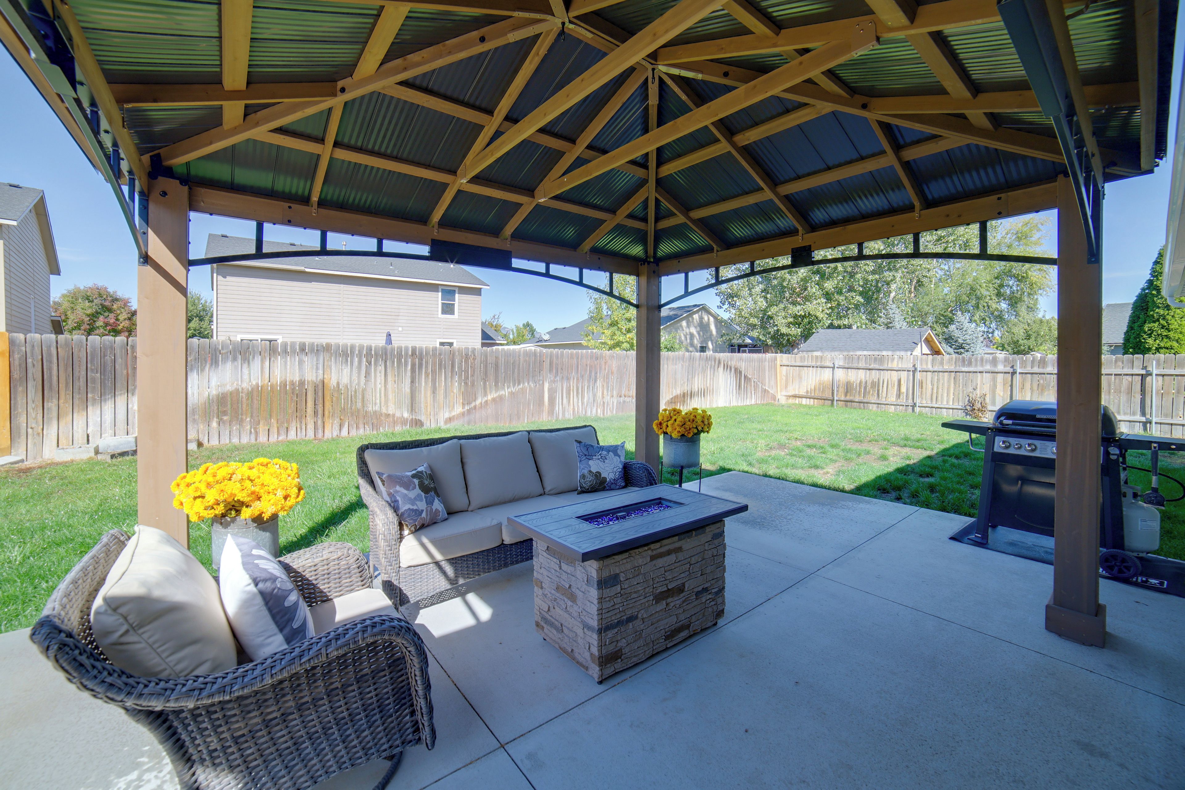 A covered patio area with a stone table, wicker furniture, and yellow flowers.