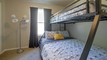 A bunk bed with a patterned bedspread and pillows, a standing floor lamp, and a window with curtains.