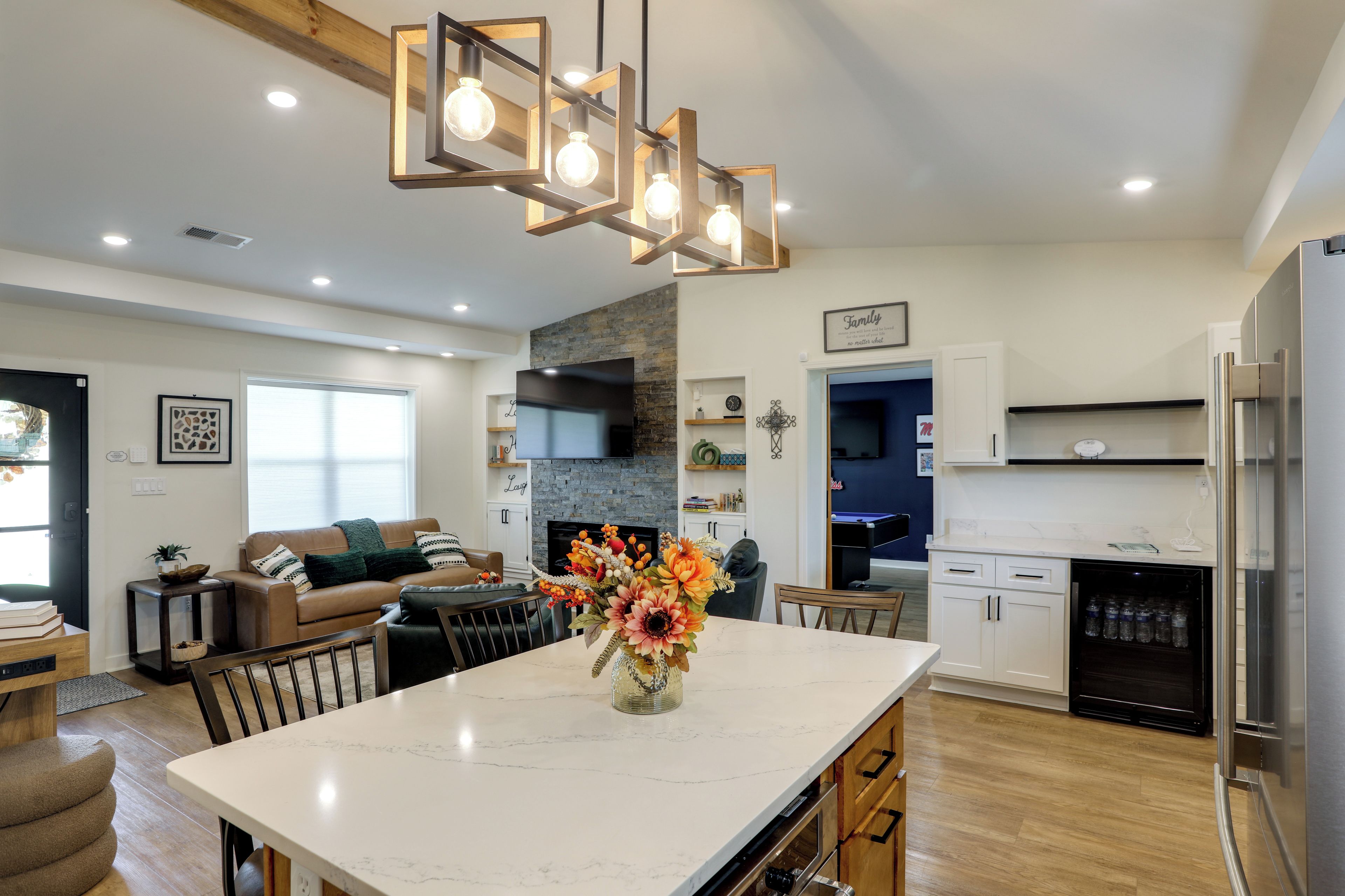 A modern kitchen with a marble island, stainless steel appliances, and a dining area with a vase of flowers.
