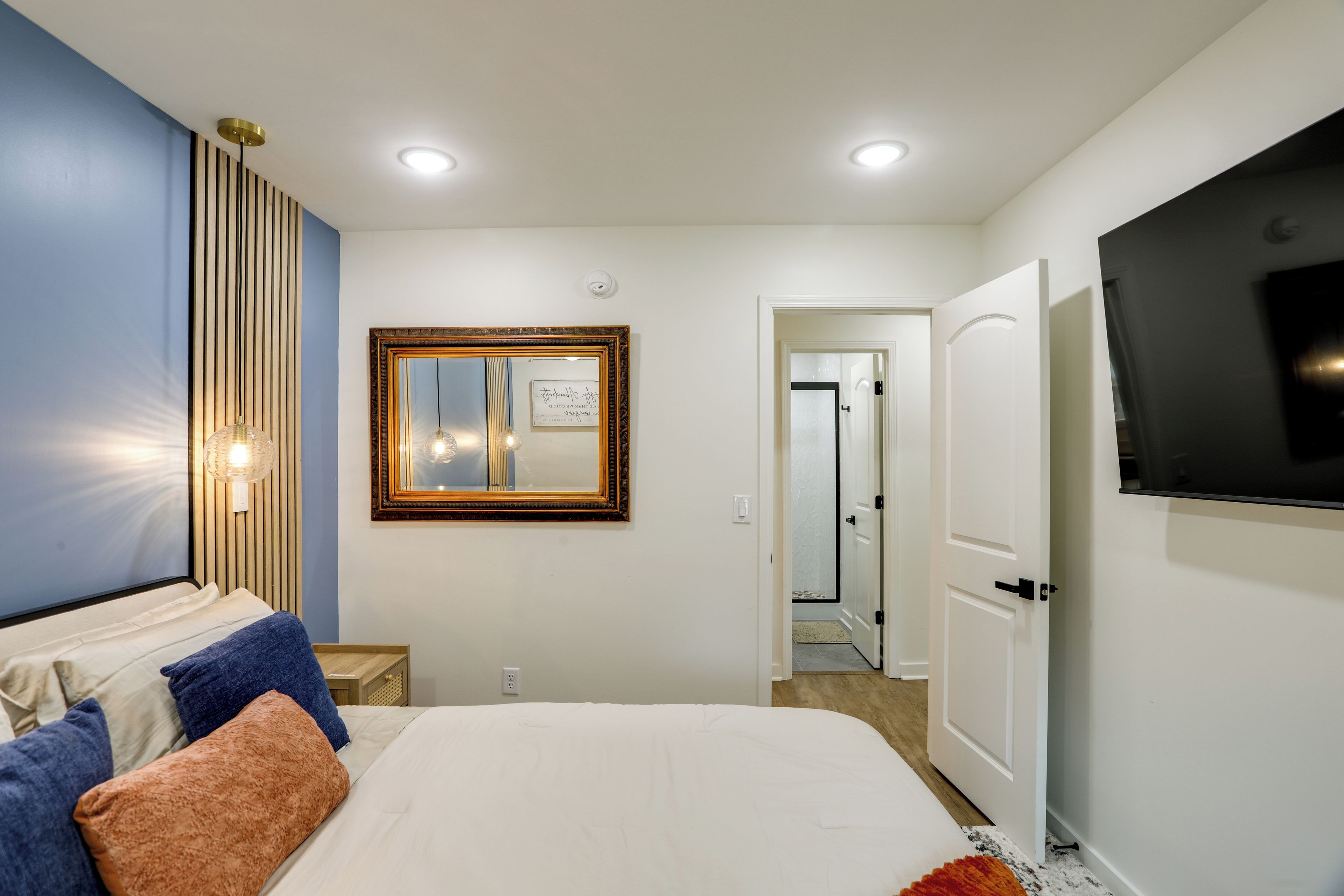 Une chambre à coucher comprenant un lit, un téléviseur, un miroir et un luminaire fixé au mur.