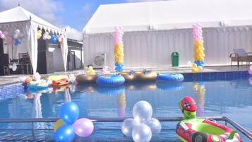 A swimming pool with inflatable toys and balloons, surrounded by a white tent structure.