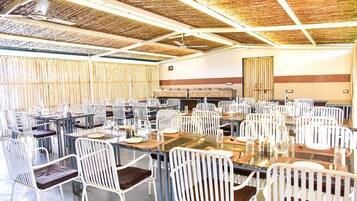 Un comedor amplio con varias mesas y sillas, un techo alto con techo de paja, y una mesa de buffet.