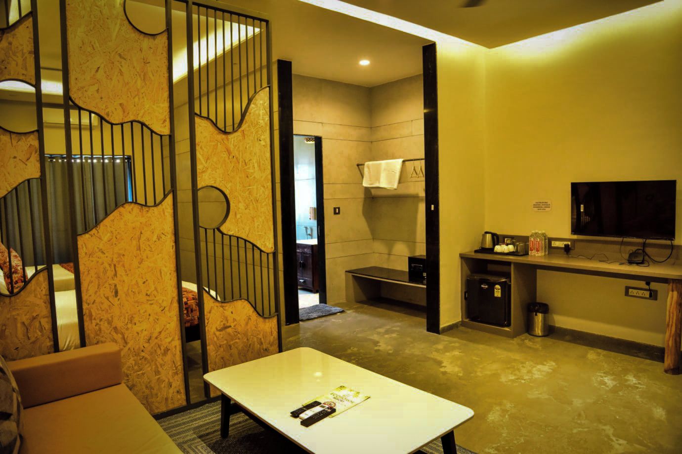 A hotel room with a white table, a TV, a kitchenette, and a bathroom visible through an open door.